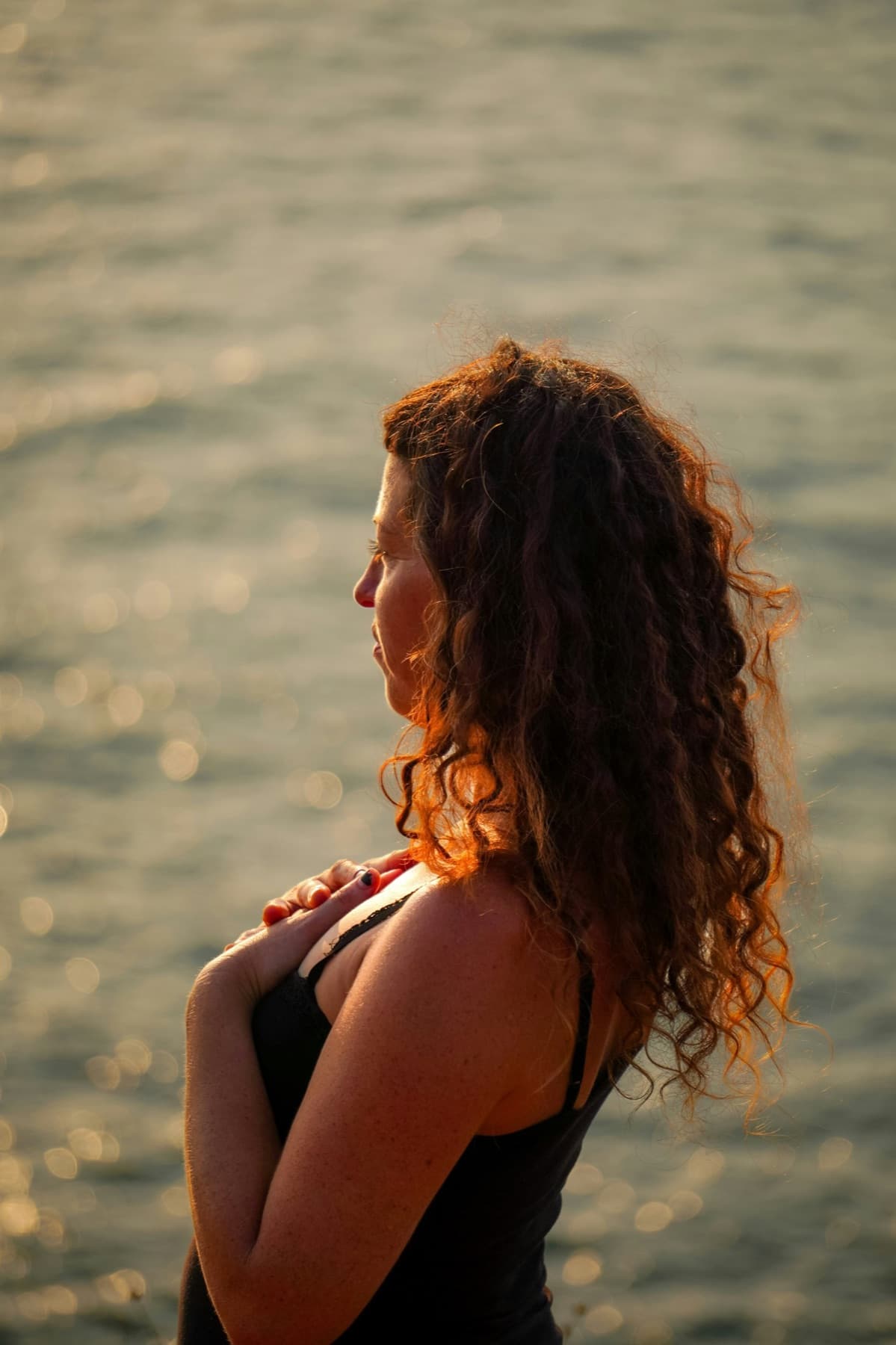 Femme de profil au bord de l'eau, une main posée sur le cœur, dans la lumière du soir