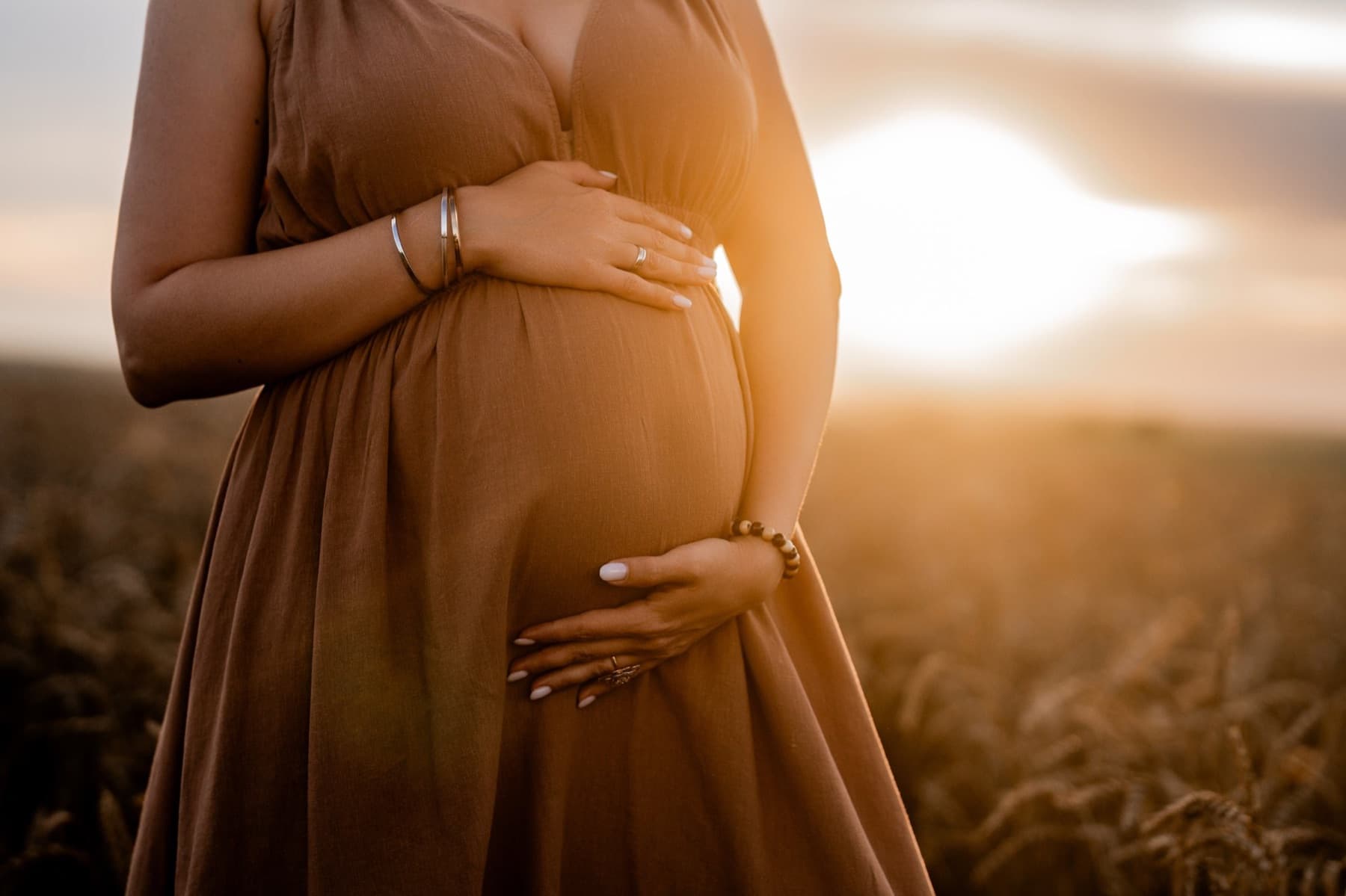 Femme enceinte tenant son ventre dans un champ, au soleil couchant
