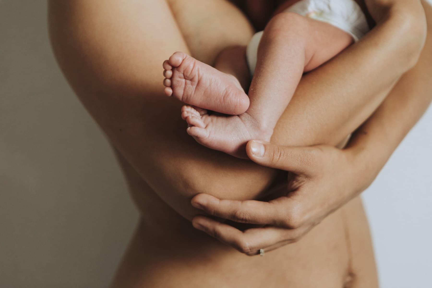 Mère tenant son nouveau-né contre elle, les pieds du bébé au creux de sa main